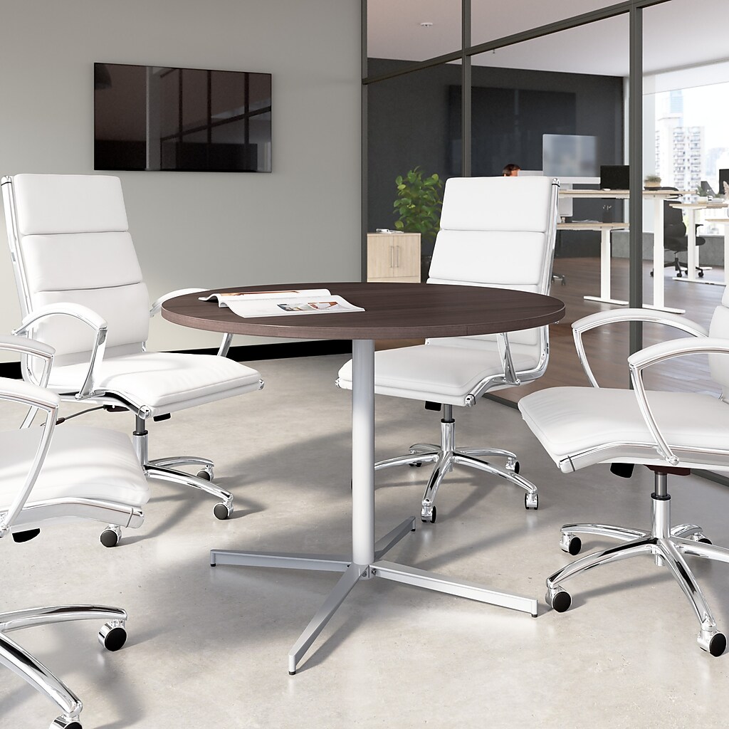 Round dark wood conference table in an office setting with white chairs