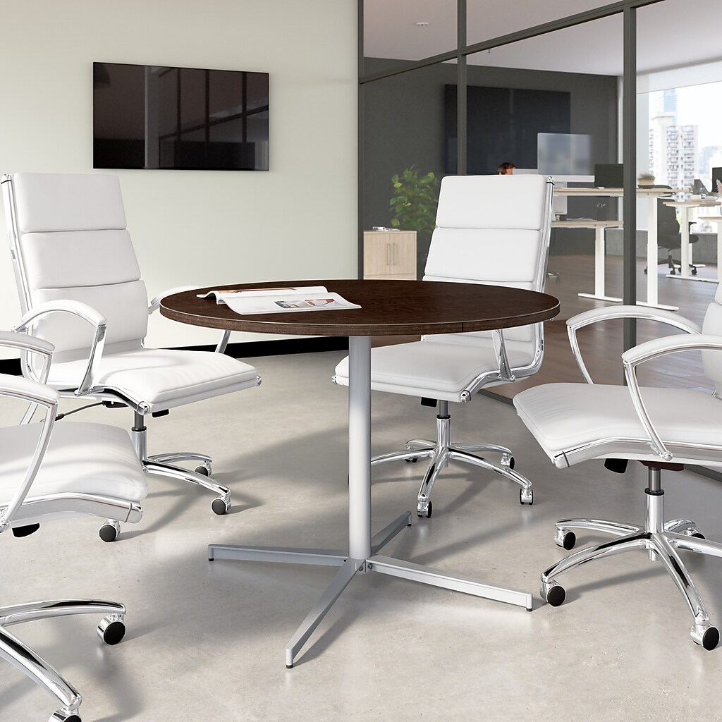 Round wood-top table in modern office surrounded by white leather chairs