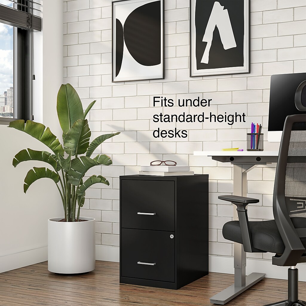 Two-drawer black filing cabinet under white-brick desk setup
